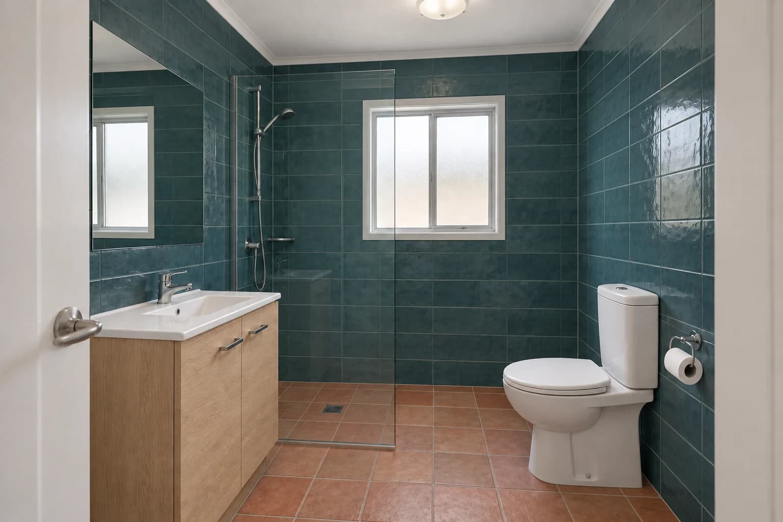 Teal tiles, an oak vanity and terracotta flooring in a compact bathroom.
